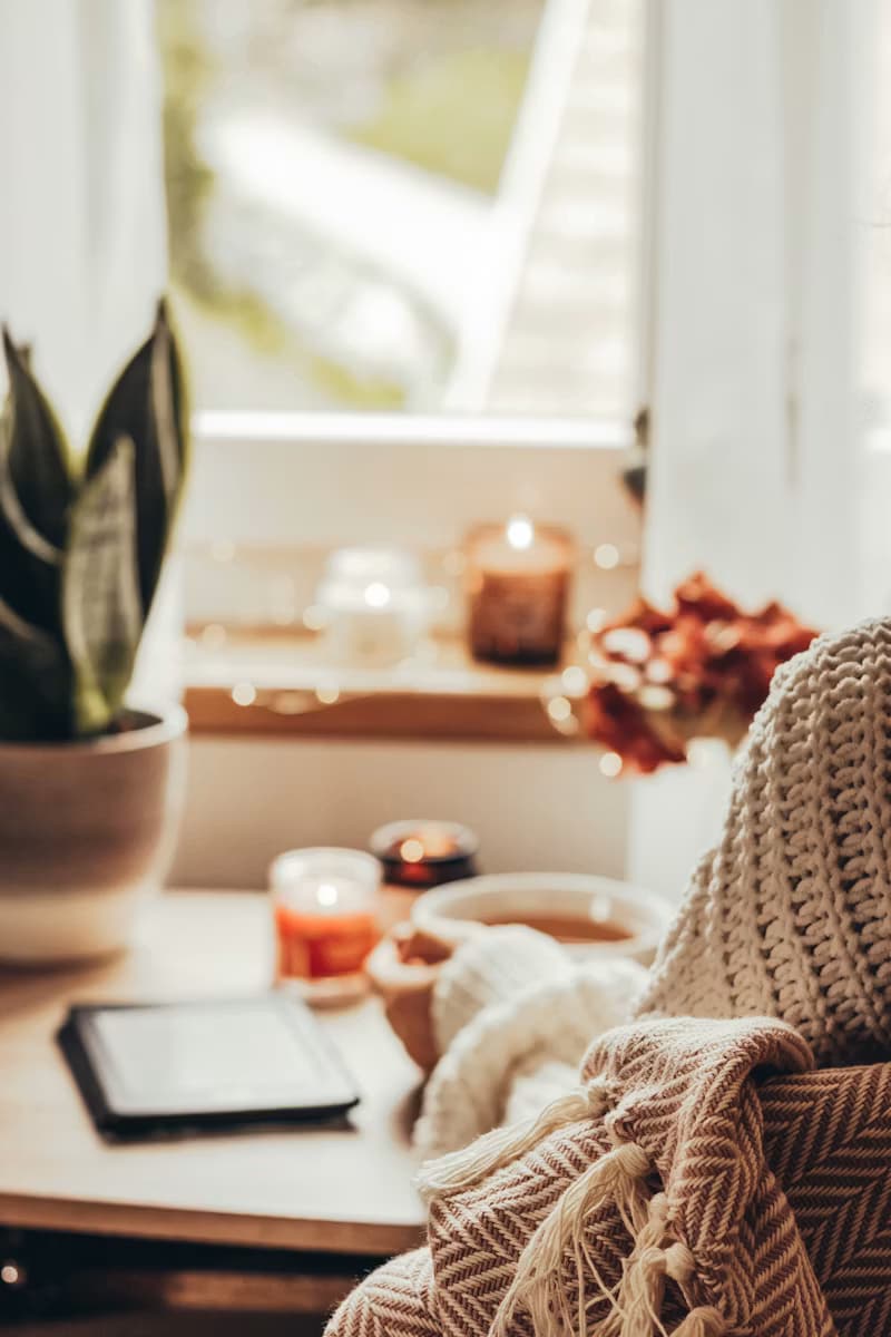 A cozy window seat with a tablet, plants, and candles, set up for an online therapy session